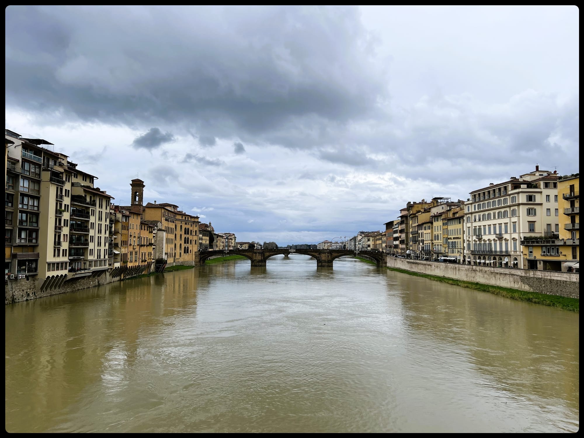 A view of the Ponte Santa Trinita over the Arno in Florence showing buildings on either side and the river in the center. Several days of rain had turned the river brown.